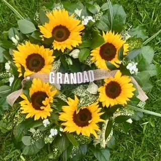 A wreath with sunflowers and a ribbon that says grandad.